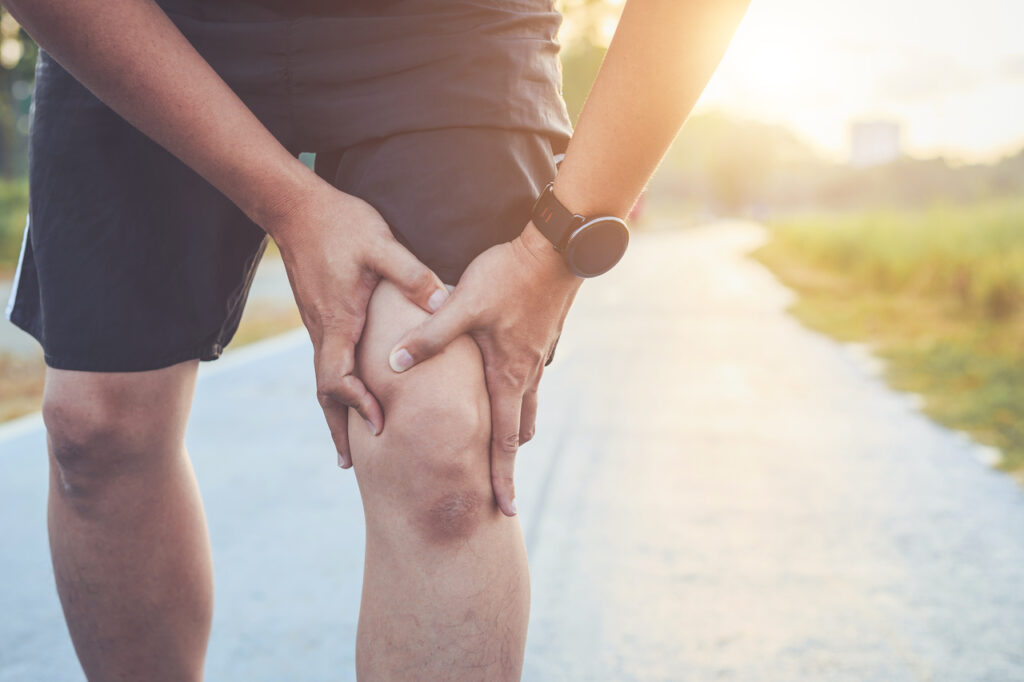 atleta segurando com a mão esquerda a região onde é a dor da síndrome do trato iliotibial