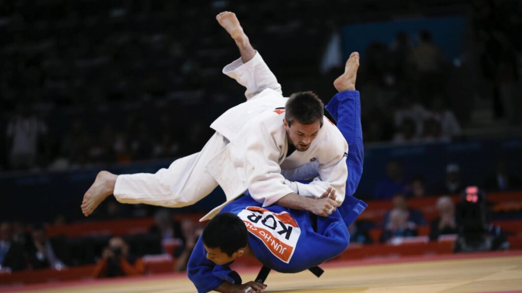 atleta de judo levando um golpe e caindo de ombro no tatame